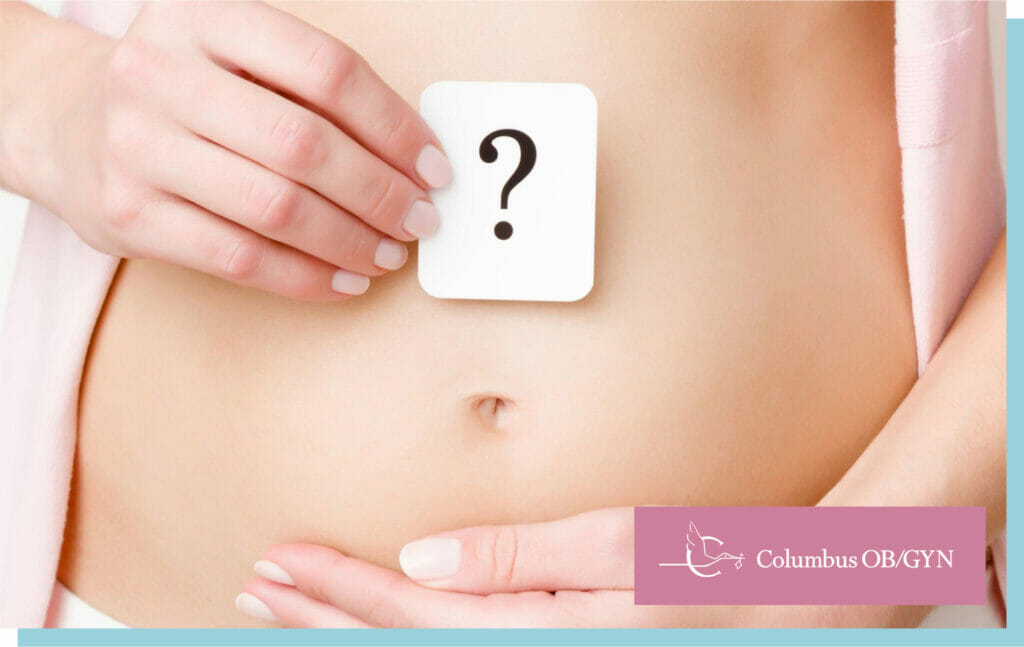 Woman showing question mark on naked belly. Gentle touch. Concept of baby planning, abdomen health or girls problems. Close up. Front view