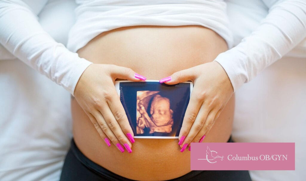 Pregnant woman holding an ultrasound image against her belly, representing prenatal care and pregnancy services at Columbus OBGYN.