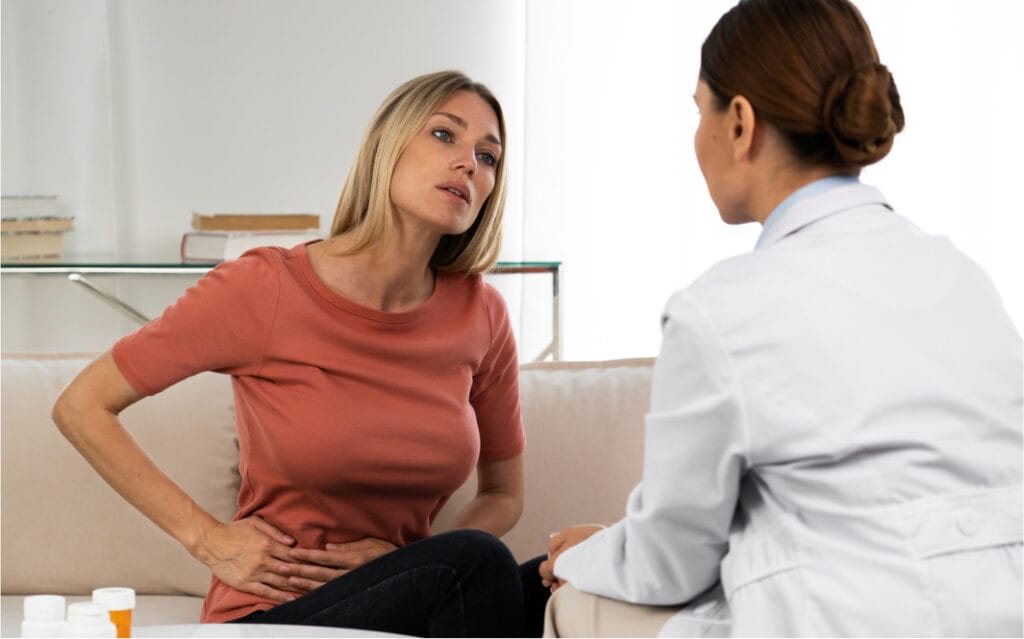A woman discussing symptoms with a doctor in a home setting, representing telehealth, home visits, or supportive gynecological care for conditions like ovarian cysts or hormonal issues